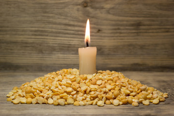 Crushed dried peas and burning candle on wooden background