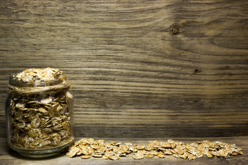 Fototapeta na wymiar Wheat flakes in glass jar on wooden background