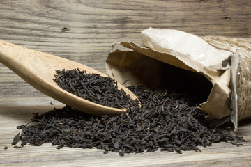 Dry tea leaves for black tea and wooden spoon on wooden background