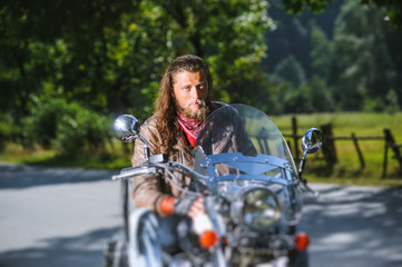 Portrait of biker with long hair and beard in a leather jacket and sunglasses sitting on his bike...
