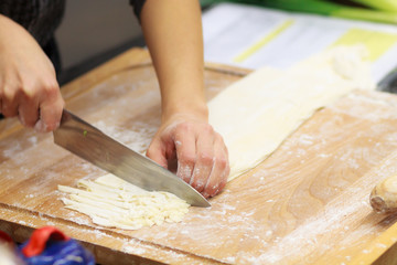Cutting dough with knife on wooden board in the kitchen