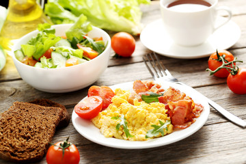 Scrambled eggs with bacon and vegetables on a grey wooden table