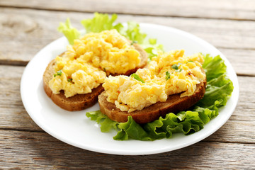 Scrambled eggs with bread and vegetables on a grey wooden table