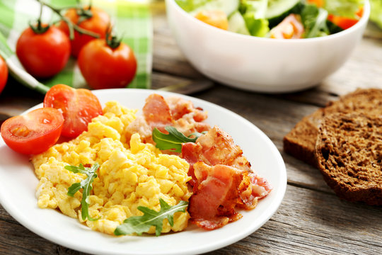 Scrambled eggs with bacon and vegetables on a grey wooden table