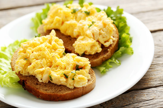 Scrambled eggs with bread and vegetables on a grey wooden table