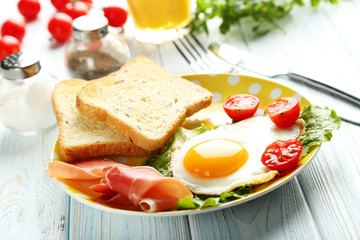 Fototapeta na wymiar Fried eggs with bacon and toasts on plate on blue wooden table