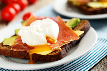 Poached eggs with avocado and bacon on toasts on grey wooden tab