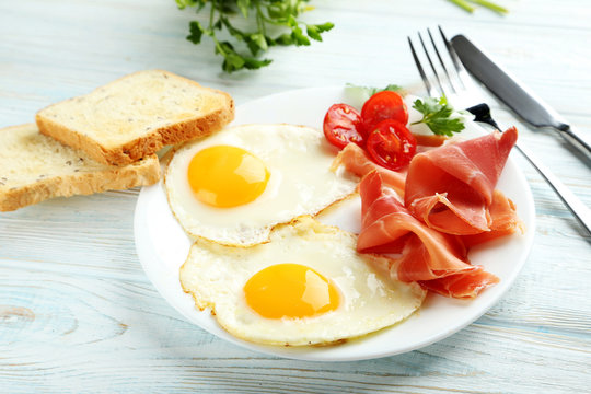 Fried eggs with bacon and toasts on plate on blue wooden table