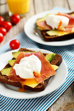 Poached eggs with avocado and bacon on toasts on grey wooden tab