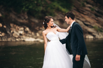 Naklejka premium Beautifull wedding couple kissing and embracing near the shore of a mountain river with stones 