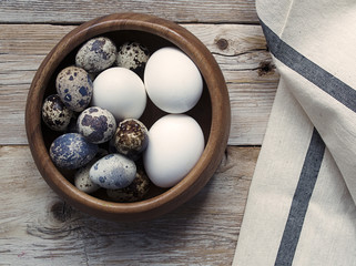 Quail and chicken eggs in a bowl on a wooden texture.