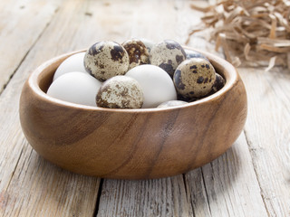 Quail and chicken eggs in wooden bowl, vintage table.
