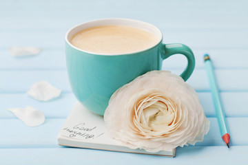 Coffee cup with spring flower and notes good morning on blue rustic background, breakfast on...