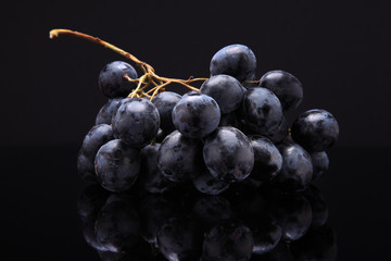 Closeup image of black grapes on black background with reflectio