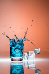 Eiswürfel fallen in ein Schnapsglas mit blauer Flüssigkeit