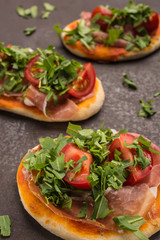 Pizza mit Rucola, Tomate und Schinken im Hochformat