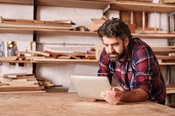 Woodwork craftsman in his studio using a digital tablet