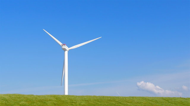 Wind turbine on the left side with a grass field in front
