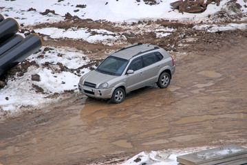 Obraz na płótnie Canvas Автомобиль-кроссовер стоит на грязной дороге на строительной площадке в оттепель зимним днем
