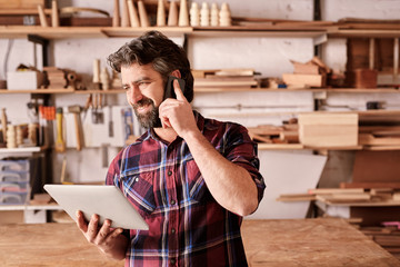 Small business owner in workshop with phone and digital tablet