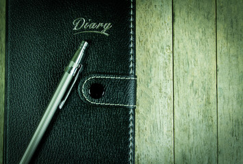 Diary notepad and pen on wood background, vintage vignette added