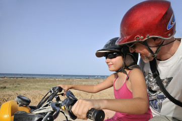 Little girl driving an ATV quad bike with her dad by sea