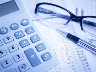 Business concept with calculator,pen,glasses and financial documents in blue light.