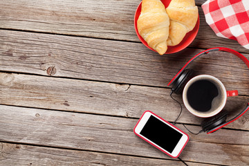 Fresh croissants, coffee, smartphone and headphones