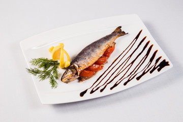 Baked fish with tomato on white plate on light background
