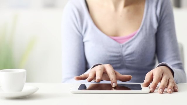 Woman sitting at desk and using a digital touch screen tablet, she is scrolling the screen with her finger