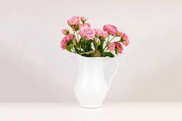 Pink flowers in white jug. Roses in jug.