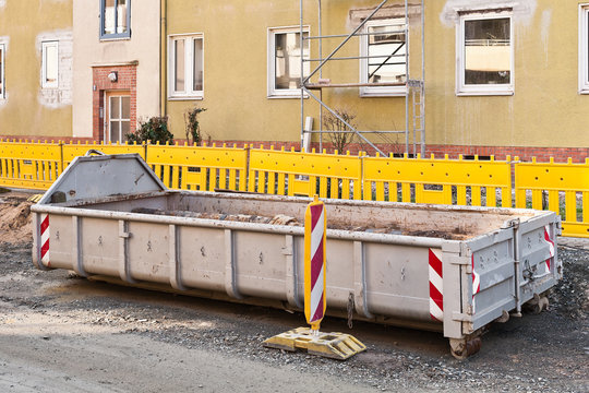 Ein grosser grauer Rollcontainer f&uuml;r Bauschutt vor gelben Baken