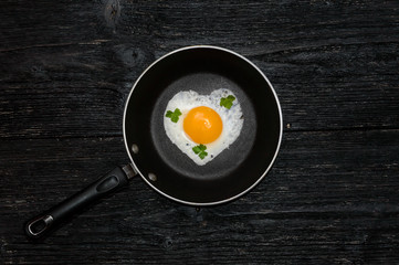fried eggs in heart shape in the pan on the wooden bachground