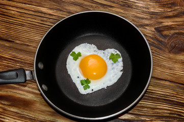 fried eggs in heart shape in the pan on the wooden bachground