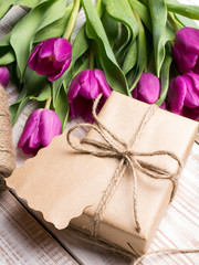 Gift box and tulips bouquet on white wooden background - retro style
