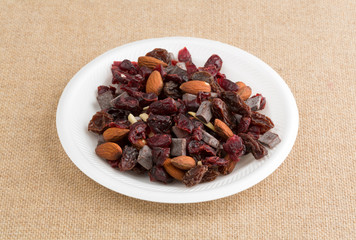 Chocolate plus nuts and cranberry trail mix on a white foam plate atop a burlap tablecloth