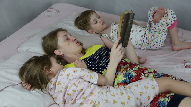 Mom reading the book to son and daughter bedtime, they lie on the bed
