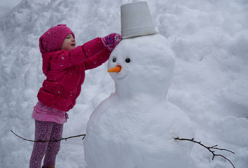 little girl wears a bucket on her head snowman