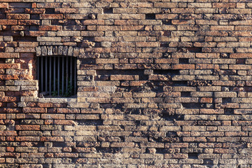 Ancient brick wall, window locked with metal bars