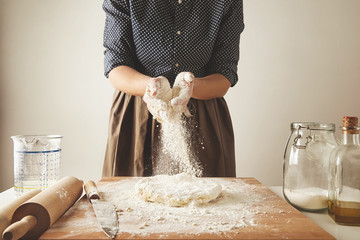 Woman adds some flour to dough on wooden table