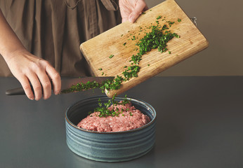 Woman hands add fresh green parsley to minced meat