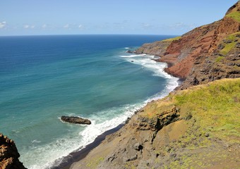 Waves crash on a black sand beach under rugged cliff