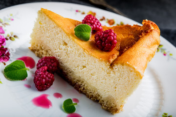 Cheesecake slice with raspberries and mint leaves on plate.