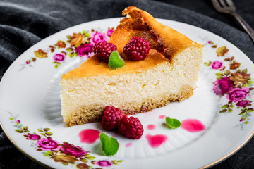 Cheesecake slice with raspberries and mint leaves on plate.