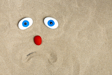 ébauche d'un visage triste dans le sable avec des galets colorés