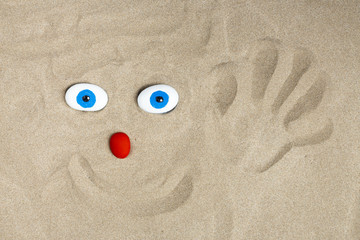 Fototapeta na wymiar Un personnage joyeux dessiné dans le sable avec des galets et des empreintes