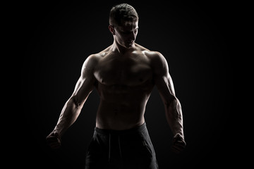 Sexy muscular man posing with naked torso on black background