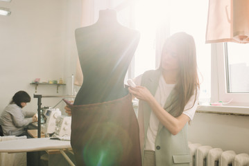 Young female fashion designer working on garment on dressmaker's model