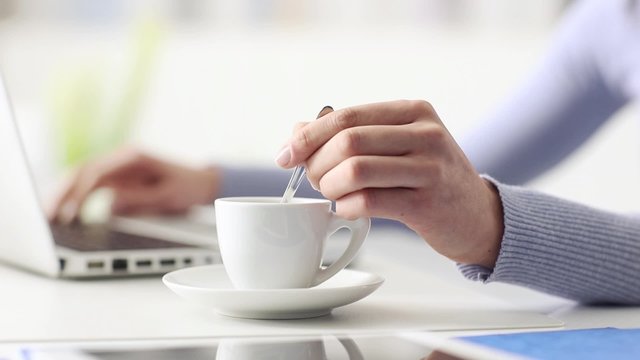 Young woman having a coffee break, she is stirring her espresso and using a laptop, hand close up, seamless loop