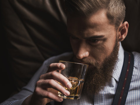 Cheerful bearded businessman is drinking expensive whisky